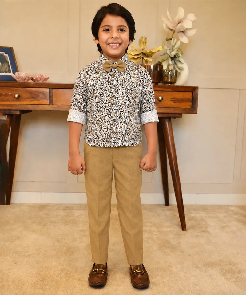 Child wearing a patterned shirt and beige pants standing in a room with wooden furniture and decorative items.