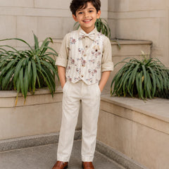 Young boy in formal attire standing outdoors with plants in the background