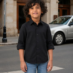 Child wearing a black shirt and blue jeans standing on a street with a car and building in the background.