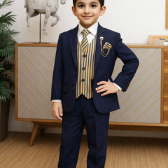 Young boy in a formal navy suit with a striped tie standing indoors.