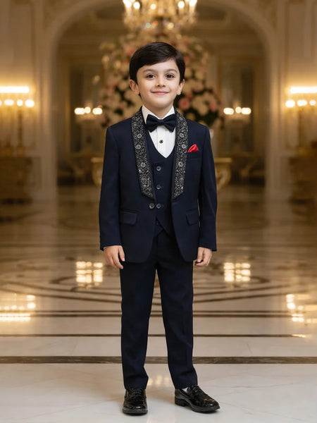 Young boy in a formal navy suit standing in an elegant room with chandeliers.