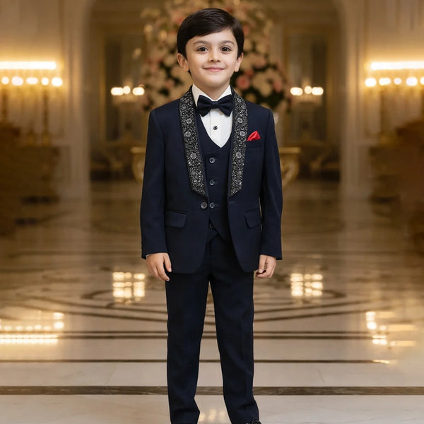 Young boy in a formal navy suit standing in an elegant room with chandeliers.