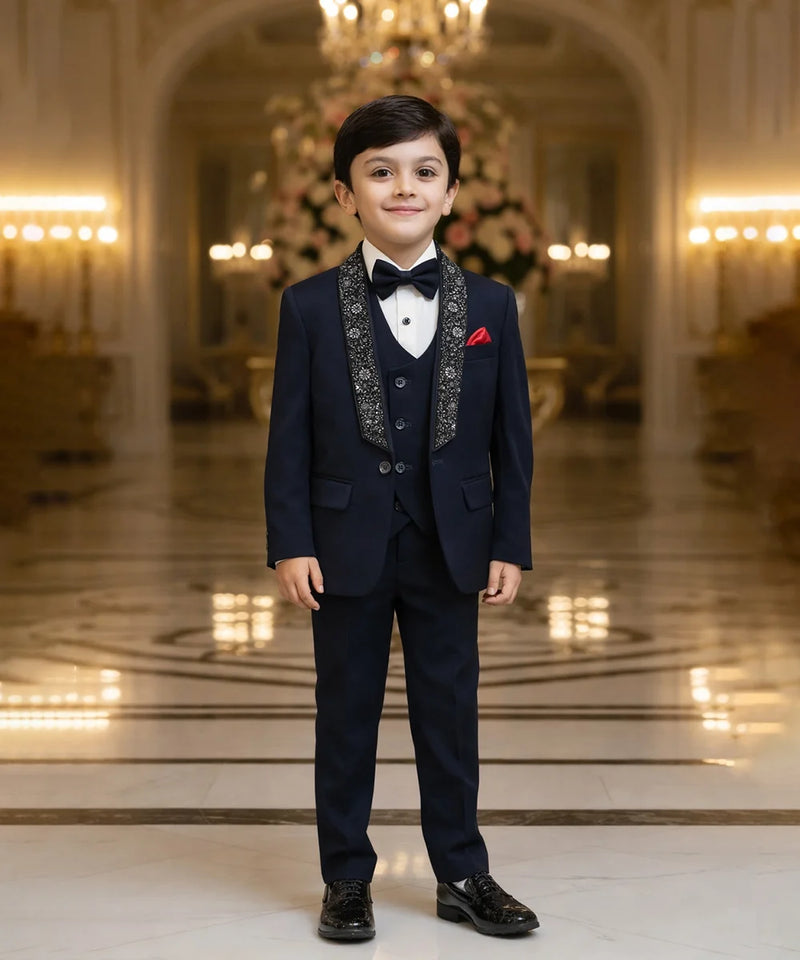 Young boy in a formal navy suit standing in an elegant room with chandeliers.