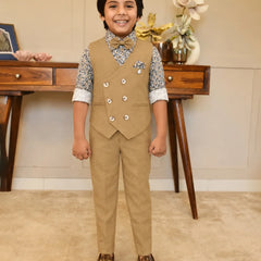 Child wearing a formal beige suit with a vest and pants, standing in a room with a wooden desk and decorative items.
