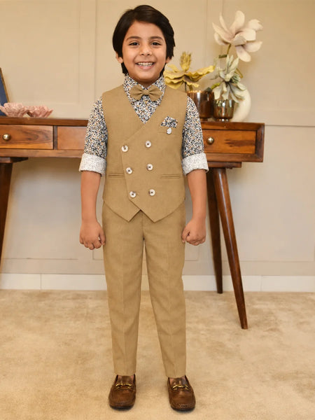 Child wearing a formal beige suit with a vest and pants, standing in a room with a wooden desk and decorative items.