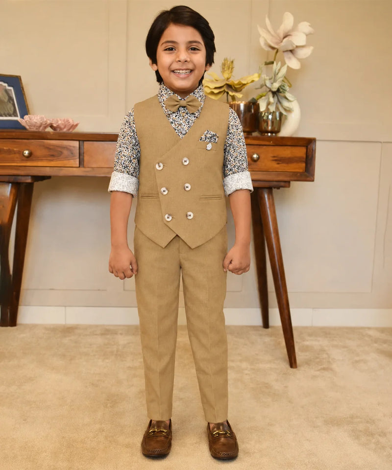 Child wearing a formal beige suit with a vest and pants, standing in a room with a wooden desk and decorative items.