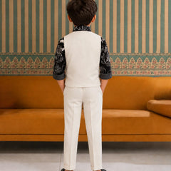 Child wearing a formal outfit standing in front of an orange sofa with striped wallpaper.