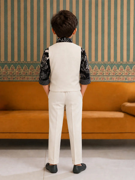 Child wearing a formal outfit standing in front of an orange sofa with striped wallpaper.