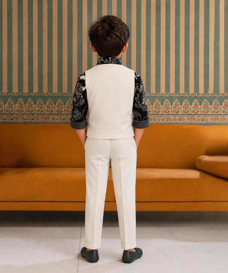 Child wearing a formal outfit standing in front of an orange sofa with striped wallpaper.