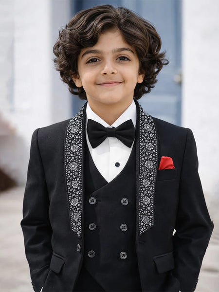boy in a black suit with a bow tie standing outdoors.