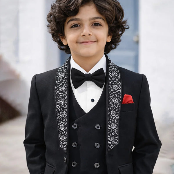 boy in a black suit with a bow tie standing outdoors.