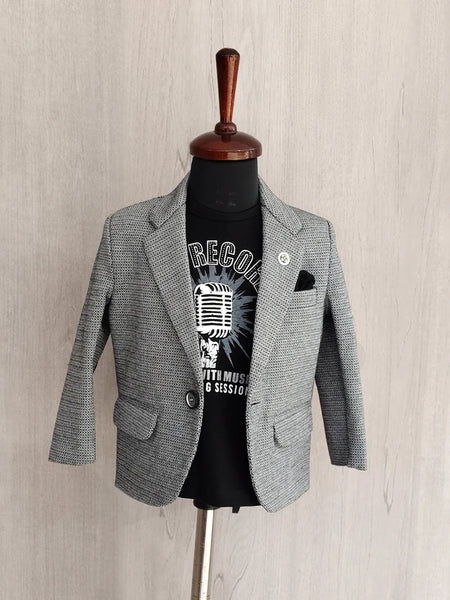 Gray blazer over a black t-shirt with graphic design on a mannequin against a beige wall.