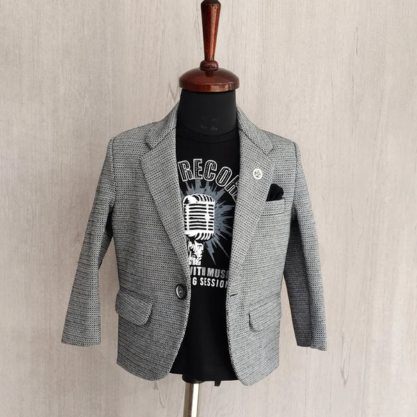 Gray blazer over a black t-shirt with graphic design on a mannequin against a beige wall.
