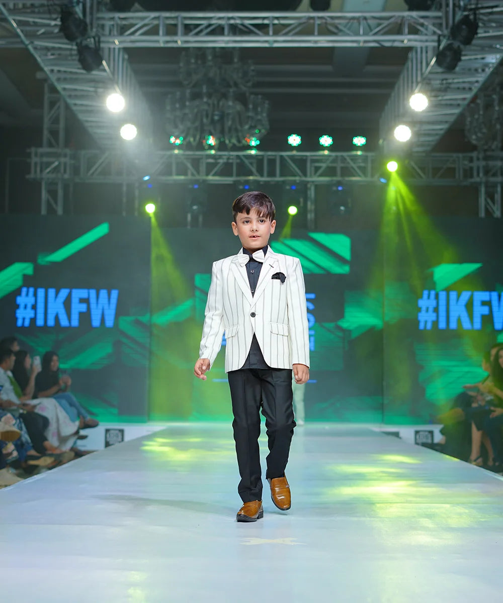 It is a classic formal party wear suit set that comes with a black shirt, pants and cream striped blazer for boys. It features a broach, a striped bow and pockets on both sides. 