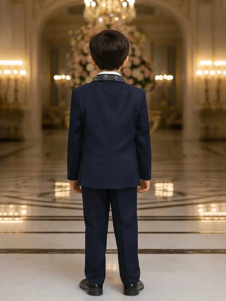 Child in a navy suit standing in an elegant room with chandeliers.