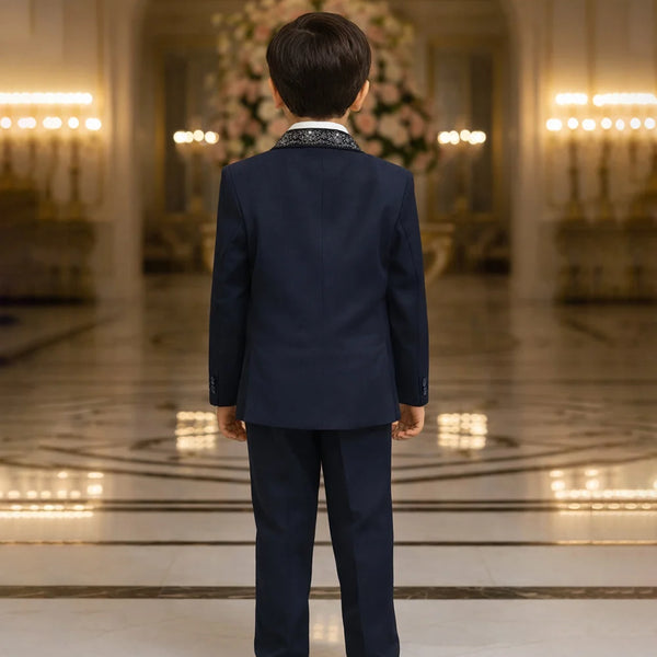 Child in a navy suit standing in an elegant room with chandeliers.