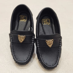 Pair of black loafers with gold tiger emblem on a beige background