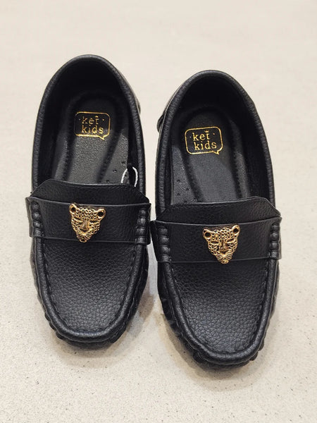Pair of black loafers with gold tiger emblem on a beige background