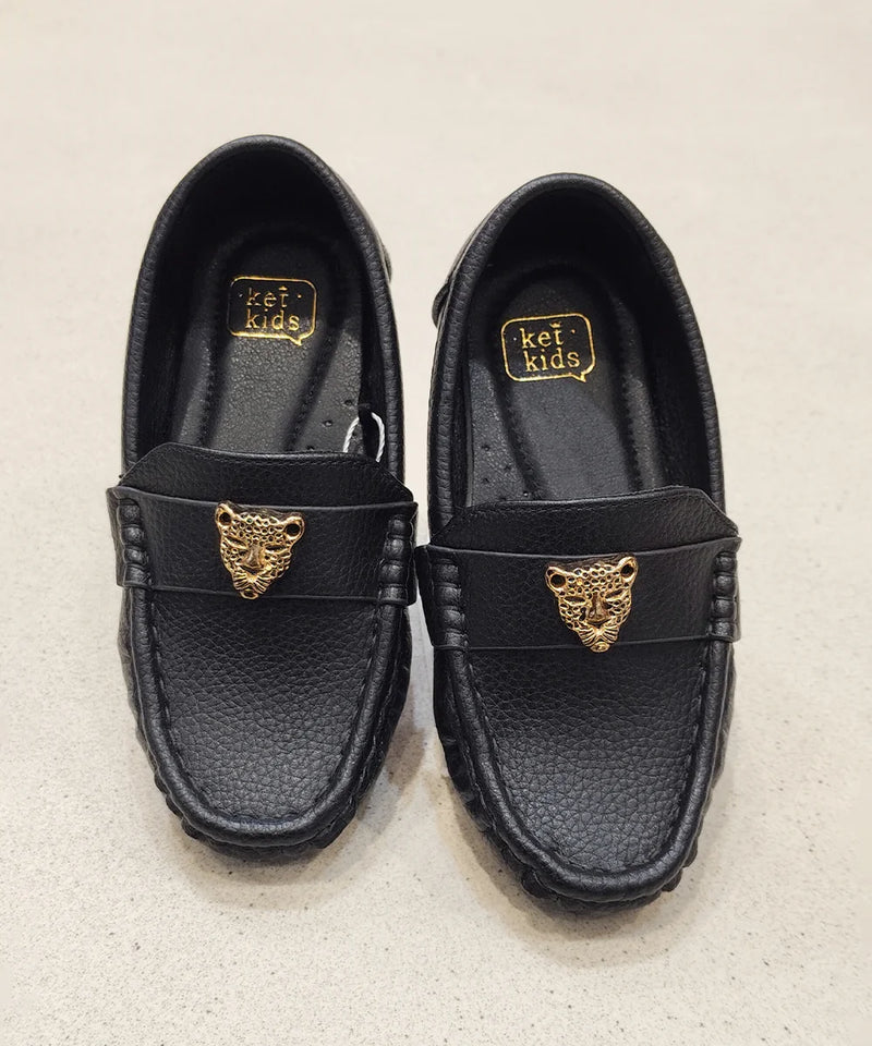 Pair of black loafers with gold tiger emblem on a beige background