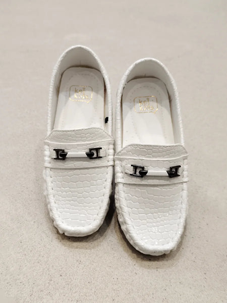 Pair of white loafers with metal buckles on a light gray background