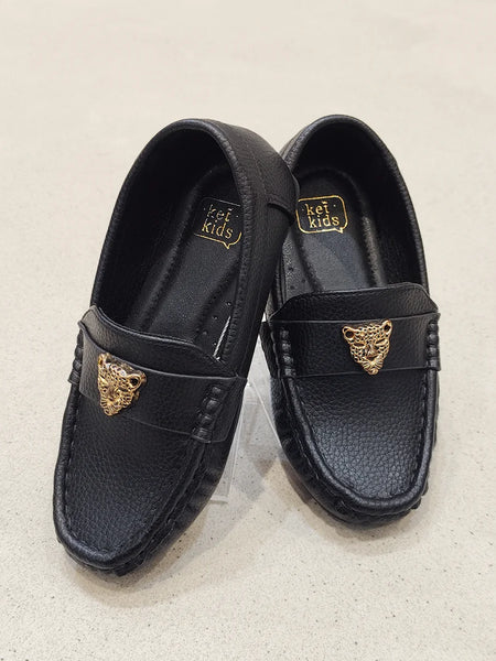 Black loafers with gold accents on a light beige background