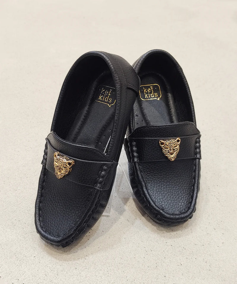 Black loafers with gold accents on a light beige background