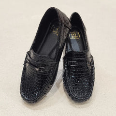 Pair of black loafers with crocodile texture on a light beige background