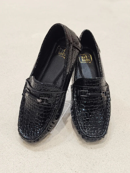 Pair of black loafers with crocodile texture on a light beige background