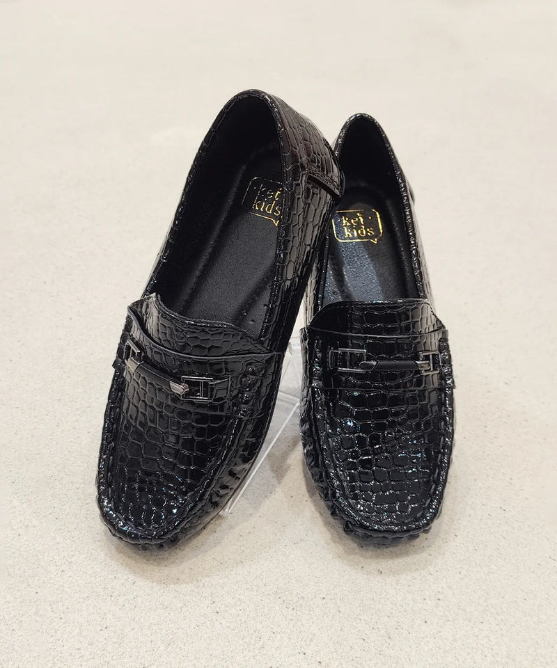 Pair of black loafers with crocodile texture on a light beige background