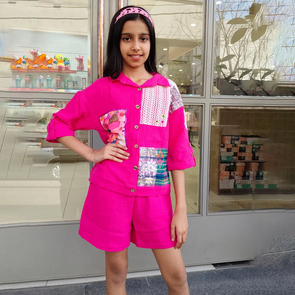 Girl wearing a bright pink outfit with colorful patches standing in front of a store.