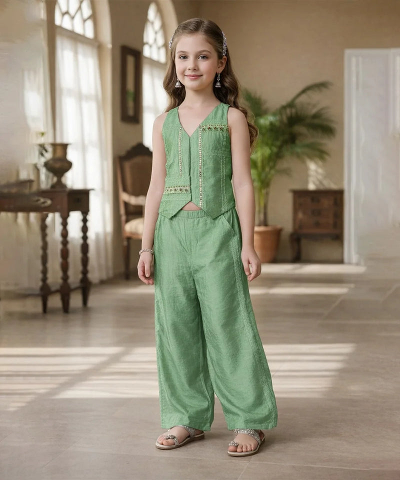 Young girl in a green outfit standing in a well-lit room with wooden floors and large windows.