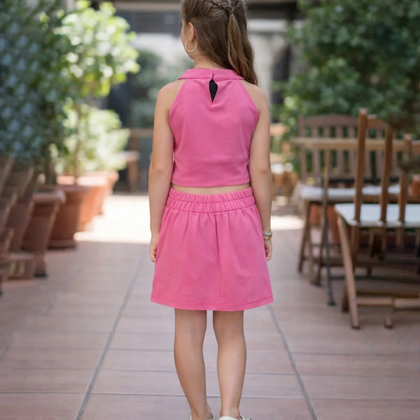 Young girl in a pink dress standing on a patio with plants and furniture in the background