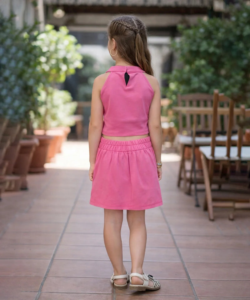 Young girl in a pink dress standing on a patio with plants and furniture in the background