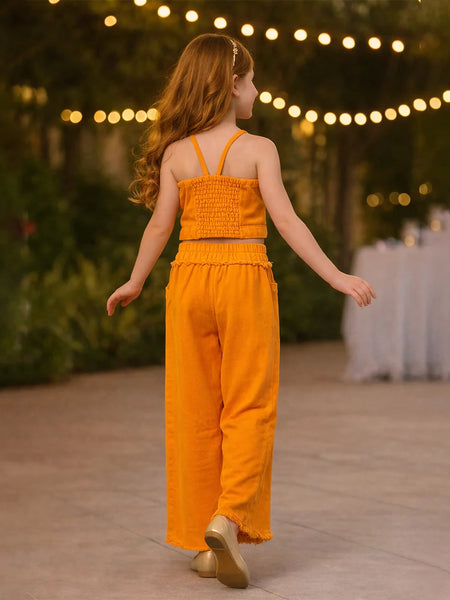 Young girl in an orange jumpsuit standing outdoors with string lights in the background