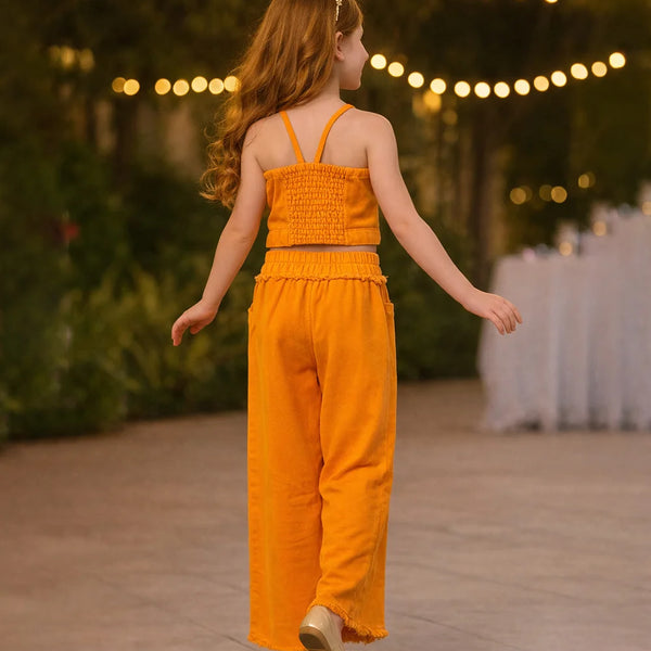 Young girl in an orange jumpsuit standing outdoors with string lights in the background