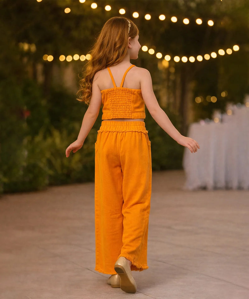 Young girl in an orange jumpsuit standing outdoors with string lights in the background