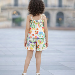 Child wearing a colorful floral dress standing on a paved surface with a blurred building in the background