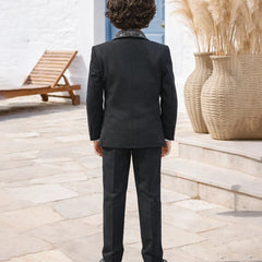 Person wearing a black suit standing outdoors with decorative elements in the background