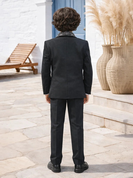 Person wearing a black suit standing outdoors with decorative elements in the background