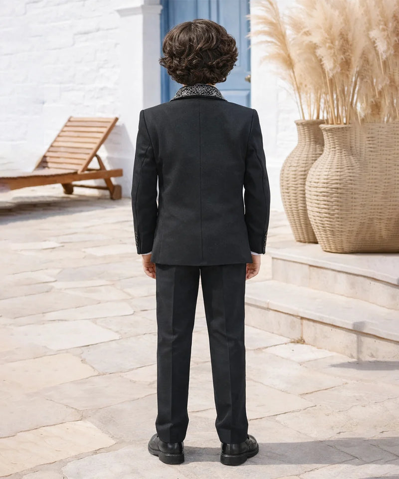 Person wearing a black suit standing outdoors with decorative elements in the background