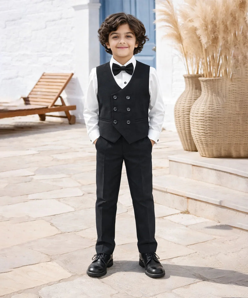 boy in a formal black suit with a bow tie standing outdoors.