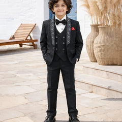 Young boy in a formal black suit with a bow tie standing outdoors.