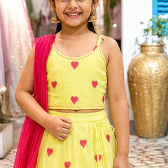 Young girl wearing a yellow outfit with pink hearts, standing indoors.