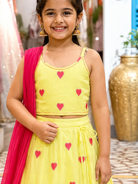 Young girl wearing a yellow outfit with pink hearts, standing indoors.