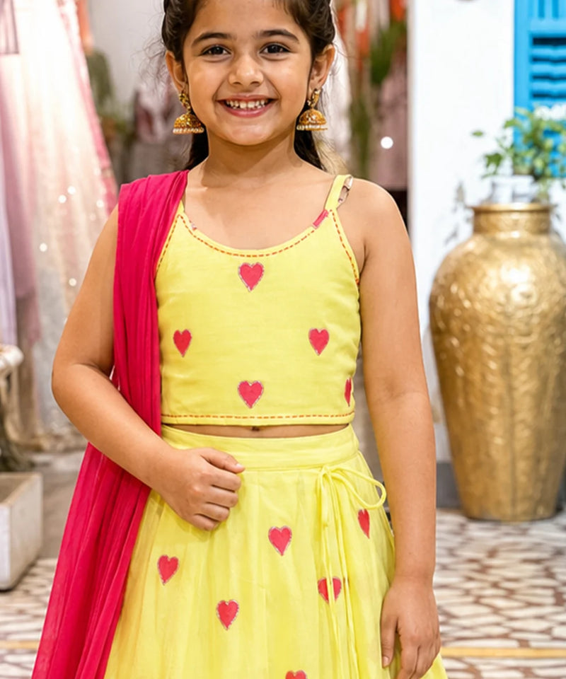 Young girl wearing a yellow outfit with pink hearts, standing indoors.
