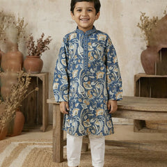 Young boy wearing a blue patterned kurta with white pants in a rustic setting.