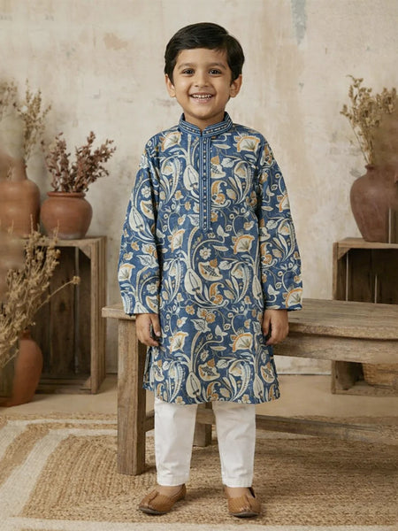 Young boy wearing a blue patterned kurta with white pants in a rustic setting.