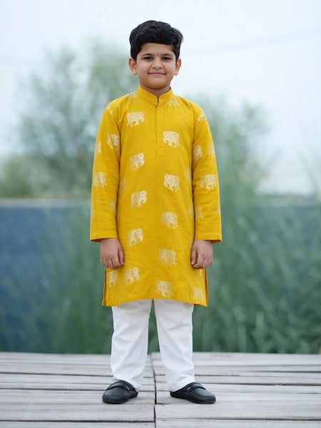 Child wearing a yellow kurta with white patterns on a wooden platform with a blurred natural background