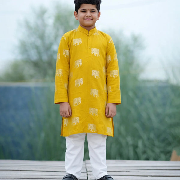 Child wearing a yellow kurta with white patterns on a wooden platform with a blurred natural background