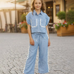Young girl in a blue outfit standing on a cobblestone street.